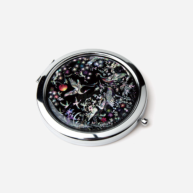 검은 옻칠 바탕 위에 자개 상감으로 송학과 꽃, 구름 문양을 섬세하게 표현한 금속 테두리 원형 손거울.