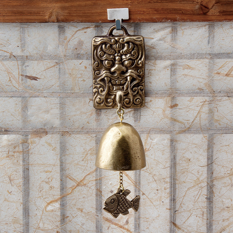 청동빛 금속 재질의 도깨비 얼굴 장식과 물고기 장식이 매달린 종 형태의 전통 풍경 장식.