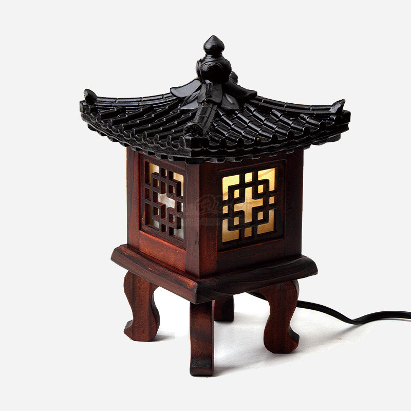 목재로 제작된 정자 형태 좌등, 흑색 기와 지붕과 사각 완자문 창살, 은은한 노란 조명 대비가 특징인 조명 장식.