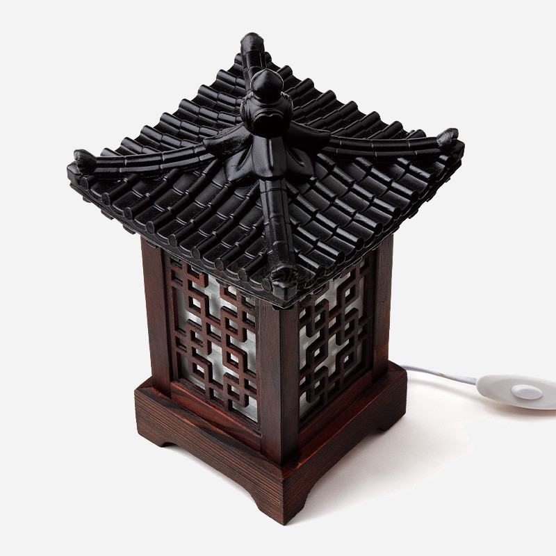 기와 지붕 형태의 흑색 상단과 짙은 목재 프레임, 기와완자문 격자 문양이 돋보이는 전통 미니 좌등.
