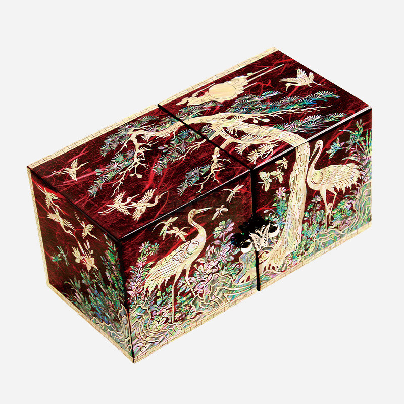 적색 옻칠 바탕에 자개 상감으로 송학과 소나무, 구름 문양을 섬세하게 표현한 직사각형 쌍합 장식품.