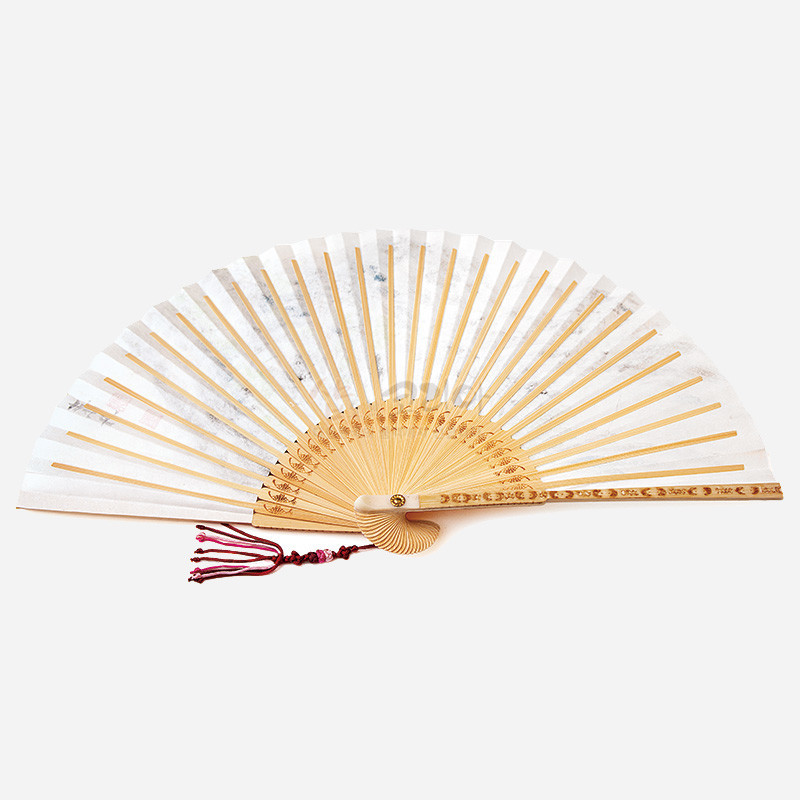 옅은 황백색 한지와 대나무 살대로 구성된 합죽선, 살대 끝 부분의 전통 문양 레이저 각인과 붉은 매듭 술 장식.