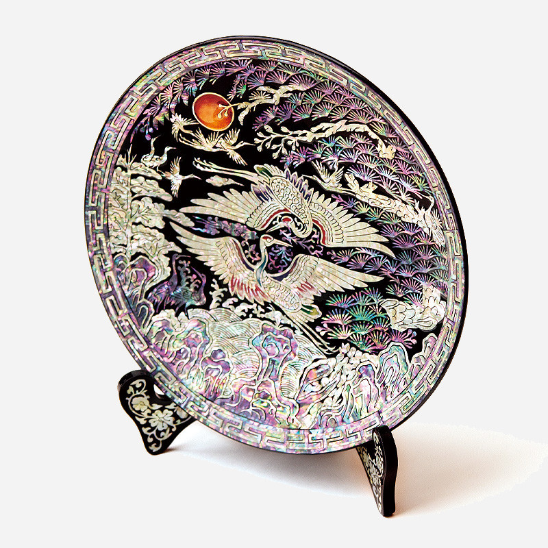 흑색 옻칠 바탕에 자개 상감 기법으로 쌍학과 송학, 일월 문양을 섬세하게 표현한 원형 쟁반형 나전칠기 오브제.