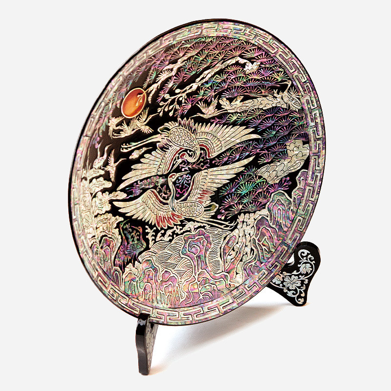 흑색 옻칠 바탕에 자개 상감 기법으로 쌍학과 송학, 일월, 구름과 파도 문양을 화려한 오방색 계열로 표현한 원형 쟁반형 오브제.