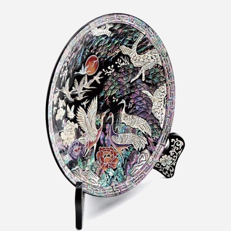 자개 상감 기법으로 송학과 소나무, 연꽃 문양을 섬세하게 표현한 흑색 옻칠 원형 쟁반 장식.