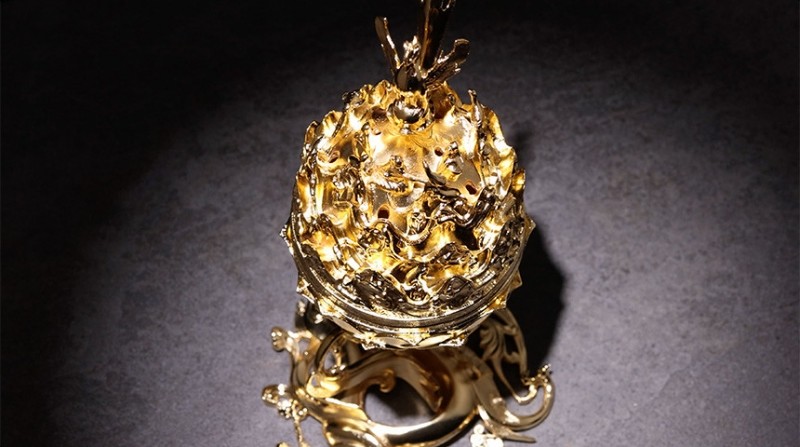 금속 재질로 제작된 금동빛 향로, 입체적인 연꽃과 산수 조각 문양, 화려한 광택 마감이 돋보이는 장식 향로.