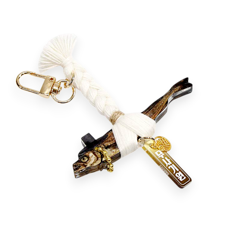 건조 명태 모양 목재에 갓 장식과 금속 장식, 흰색 전통 매듭 끈과 금색 아크릴 문양 장식을 더한 열쇠고리형 장식품.