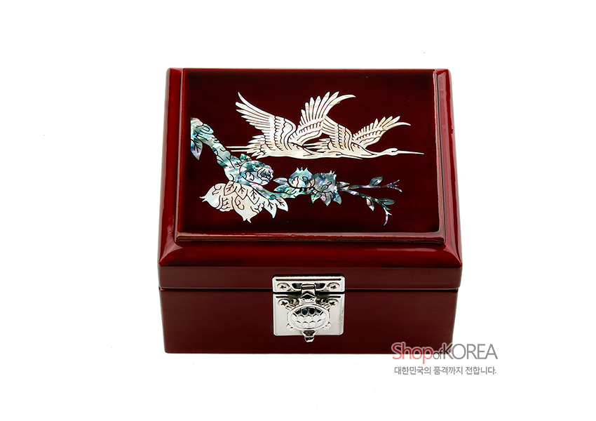 [텍스트: Shop of KOREA 대한민국의 품격까지 전합니다] 붉은 옻칠 바탕 위 자개 상감 기법으로 쌍학과 꽃나무 문양을 장식하고 은색 금속 잠금장치를 더한 사각 나전 보석함