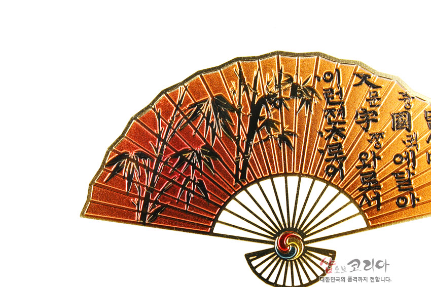 [텍스트: 샵오브코리아 대한민국의 품격까지 전합니다.] 황금빛 금속 재질 부채형 책갈피에 검은 대나무와 한글 훈민정음 서체 문양, 하단 태극 삼색 원형 장식 표현