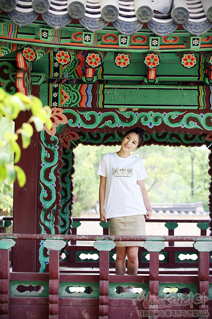 [텍스트: SHIRT OF KOREA] 전통 단청 기법의 녹색·적색 꽃문양 누각 아래, 흰색 면 티셔츠에 도깨비 캐릭터 3D 발포 프린트된 입체 효과 디자인