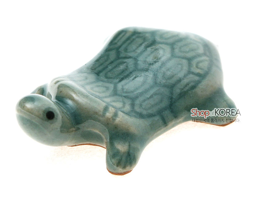 [텍스트: Shop of KOREA 대한민국의 품격까지 전합니다.] 비취색 청자 유약으로 빚은 거북이 형 수저받침, 등껍질 육각형 문양과 은은한 그라데이션 광택이 두드러지는 도자 공예품 묘사