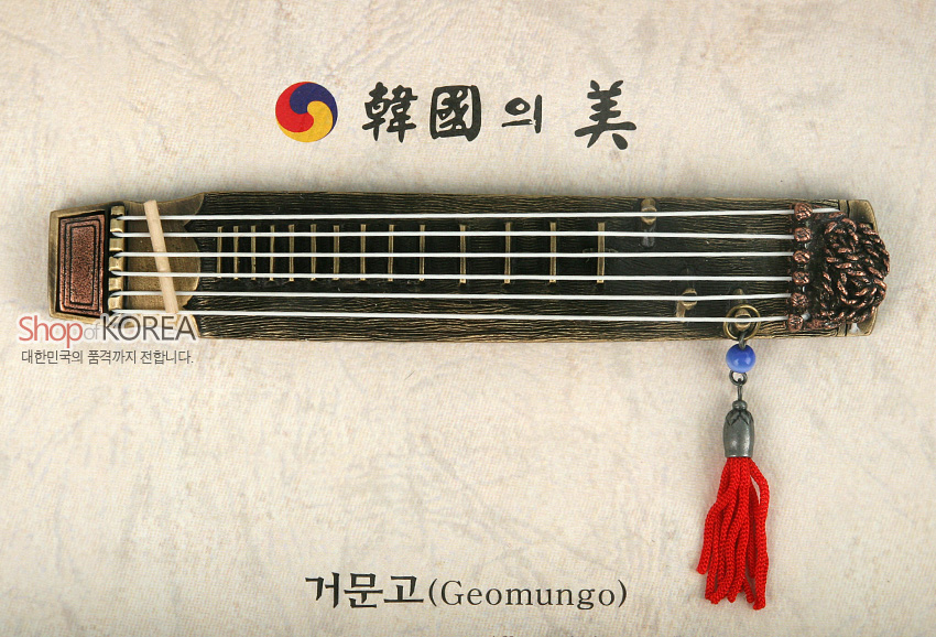 [텍스트: Shop of KOREA 대한민국의 품격까지 전합니다. 韓國의美 거문고(Geomungo)] 금속 재질 거문고 미니어처에 붉은 술 장식과 청색 구슬 포인트, 태극 문양과 서예체 글씨가 조화된 전통 악기 장식 이미지