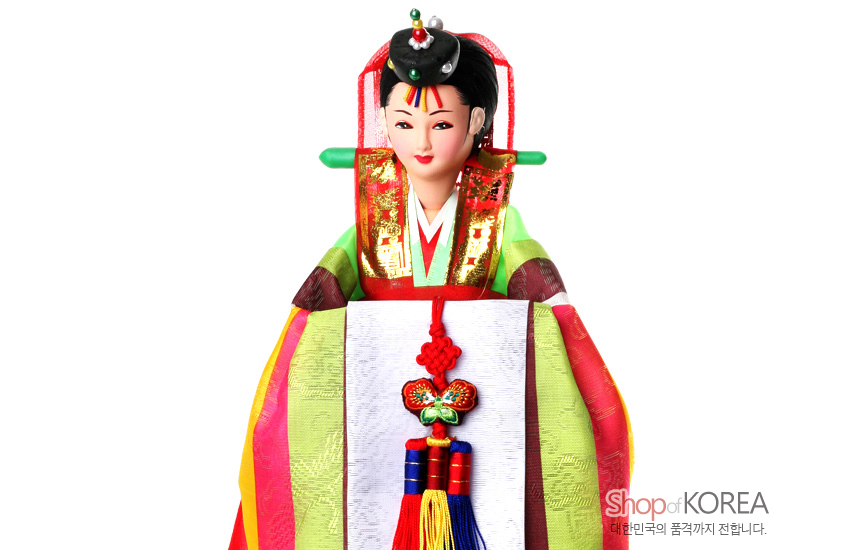 [텍스트: Shop of KOREA 대한민국의 품격까지 전합니다.] 비단 질감 연두·홍색 혼례한복과 금박 문양 장식, 오방색 술 매듭 노리개를 단 전통 신부 인형 모습