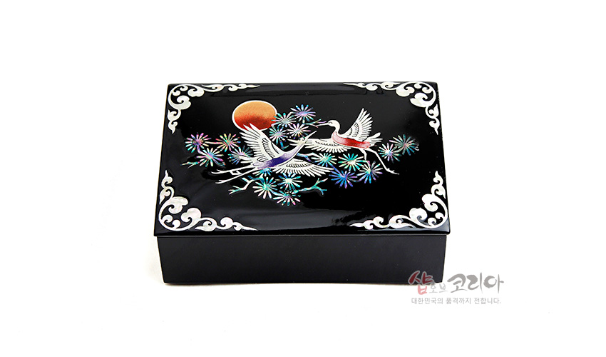 [텍스트: 샵오브코리아 대한민국의 품격까지 전합니다] 흑색 옻칠 바탕 위 자개 상감 기법으로 송학과 소나무, 붉은 해를 채색한 직사각 명함함, 모서리 백색 운문 장식 특징