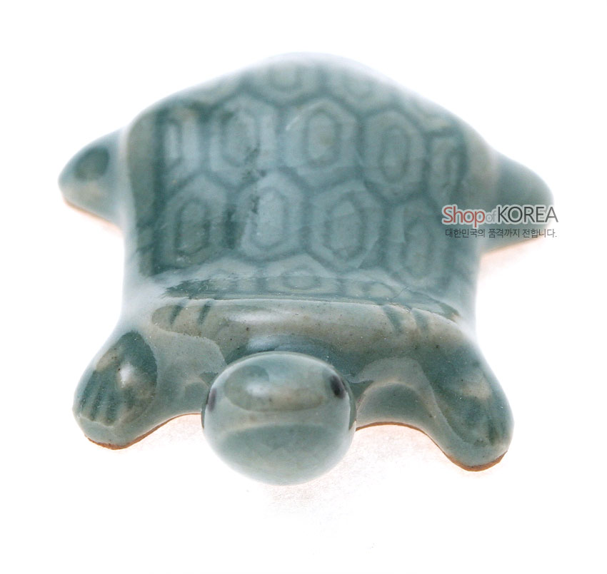 [텍스트: Shop of KOREA 대한민국의 품격까지 전합니다.] 연녹색 비취빛 청자 재질의 거북이 형태 수저받침, 등껍질 육각형 문양과 매끄러운 유약 광택이 돋보이는 도자 공예품 형상