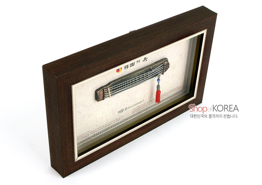 [텍스트: 國樂의 美, 거문고(Geomungo), Shop of KOREA, 대한민국의 품격까지 전합니다.] 짙은 갈색 원목 액자 속 금속 줄 표현 거문고 미니어처와 붉은 술 장식, 전통 문양 테두리 배경이 어우러진 입체 액자형 장식