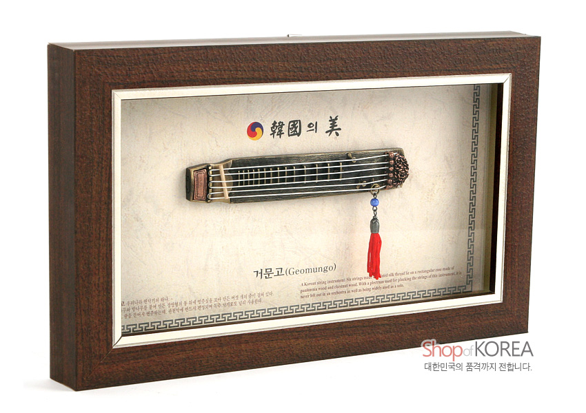 [텍스트: 韓國의 美 / 거문고(Geomungo) / Shop of KOREA 대한민국의 품격까지 전합니다.] 짙은 갈색 원목 액자 속 금속 재질 미니어처 거문고와 붉은 술 장식, 태극 문양과 전통 기하학 테두리 무늬가 조화를 이룬 전통 악기 장식 액자