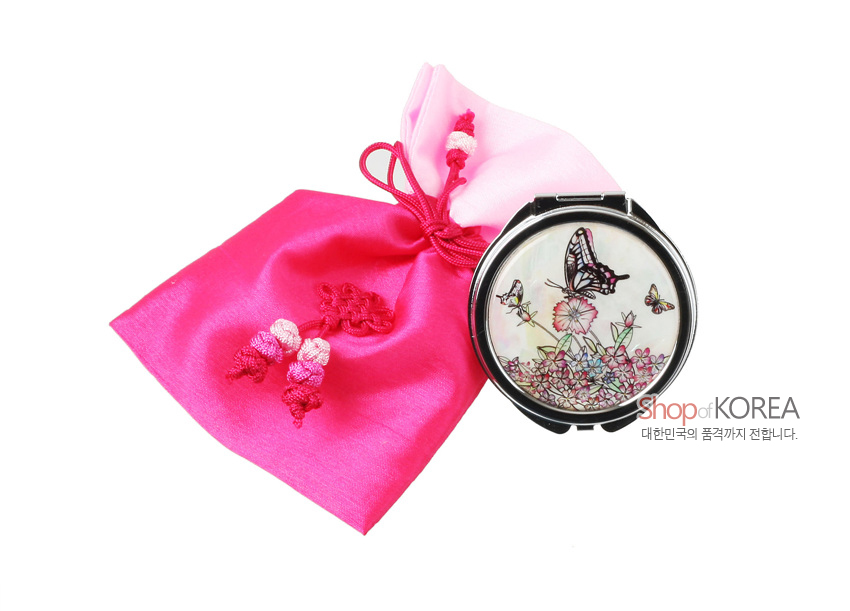 [텍스트: Shop of KOREA 대한민국의 품격까지 전합니다.] 흰 자개 바탕에 흰호랑나비와 꽃 문양을 상감한 원형 금속 손거울과 분홍색 비단 복주머니, 매듭 장식 구성