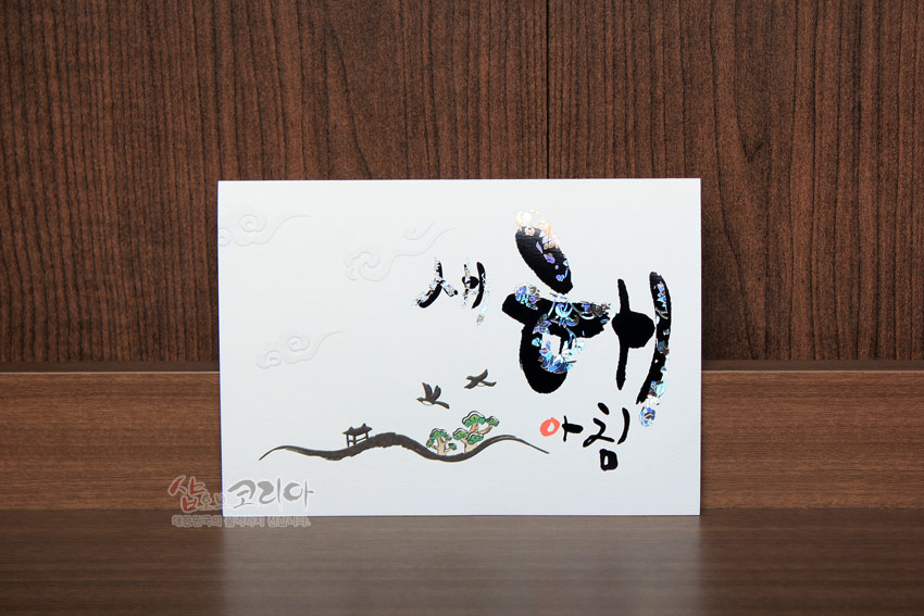 [텍스트: 새해 아침] 흰색 한지 카드 위 자개 상감 서체와 산수, 나무, 새, 구름 문양이 배치된 전통 스타일 디자인 연하장 이미지 설명