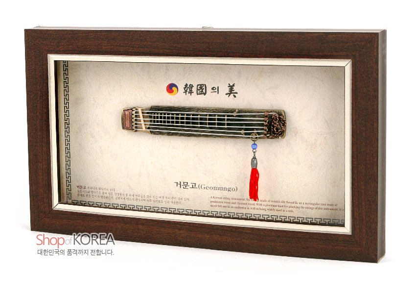 [텍스트: 韓國의 美, 거문고(Geomungo)] 짙은 갈색 나무 액자 속 금속 재질 미니어처 거문고와 붉은 술 장식, 태극 문양과 전통 기하학 테두리 문양이 어우러진 전통 악기 장식 액자 모습
