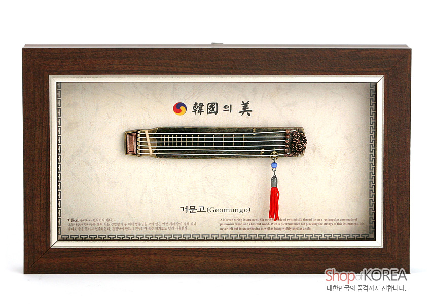 [텍스트: 韓國의 美, 거문고(Geomungo), Shop of KOREA 대한민국의 품격까지 전합니다.] 짙은 갈색 원목 액자 속 금속 재질 거문고 모형과 붉은 술 장식, 태극 문양과 전통 문양 테두리가 어우러진 전통 악기 장식 액자
