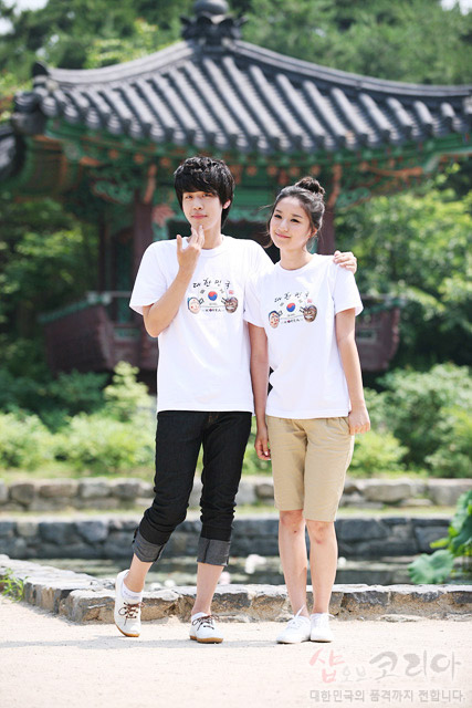 [텍스트: 샵오브코리아 대한민국의 품격까지 전합니다] 흰색 면 티셔츠 위 태극기와 전통 탈, 한글 서체가 다채로운 색상의 3D 발포 프린트로 표현된 입체 그래픽 장식 이미지