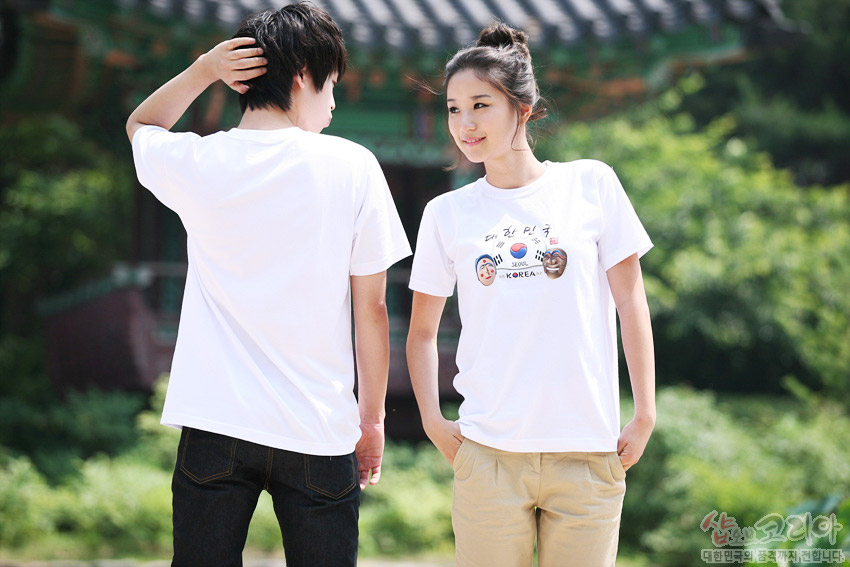 [텍스트: 대한민국 SEOUL KOREA] 흰색 면 티셔츠 위 태극기와 탈 문양, 한글 서체가 입체 발포 기법으로 표현된 전통 그래픽 디자인