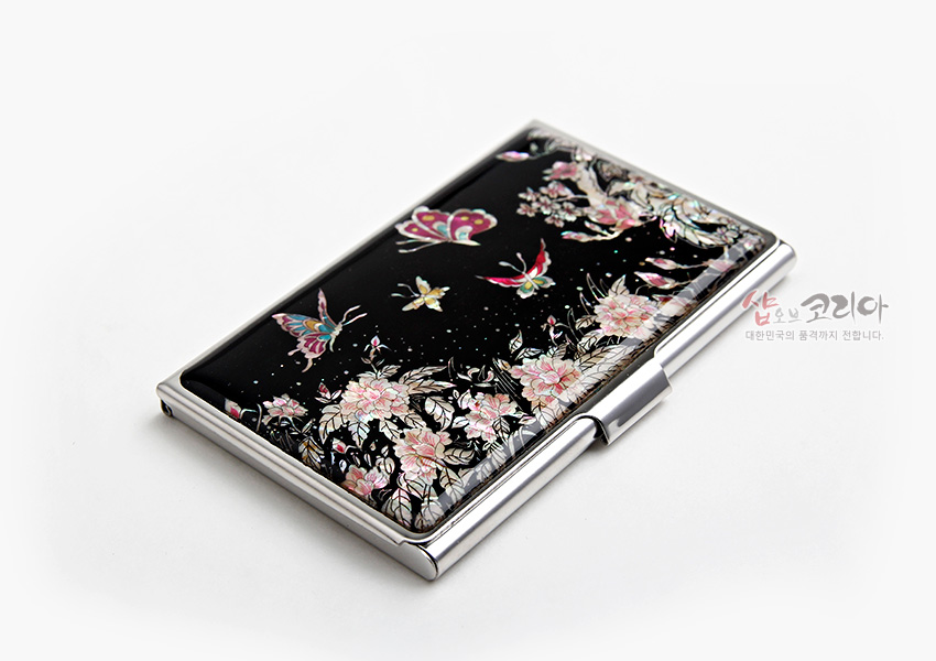 [텍스트: 샵오브코리아 대한민국의 품격까지 전합니다.] 흑색 옻칠 바탕 위 자개 상감으로 연분홍 목단꽃과 다채로운 나비 문양을 표현한 금속 명함집 이미지