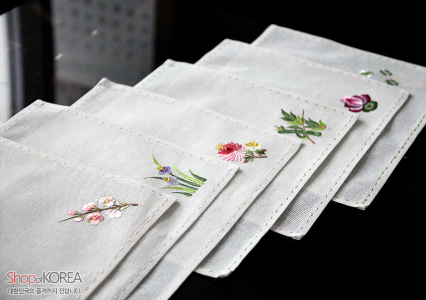[텍스트: Shop of KOREA 대한민국의 품격까지 전합니다.] 모시 재질 사각 냅킨 위에 매화·수선화·국화·대나무·연꽃 등 꽃 자수를 놓고 가장자리에 색실 스티치로 마감한 전통 자수 식탁보 세트 이미지