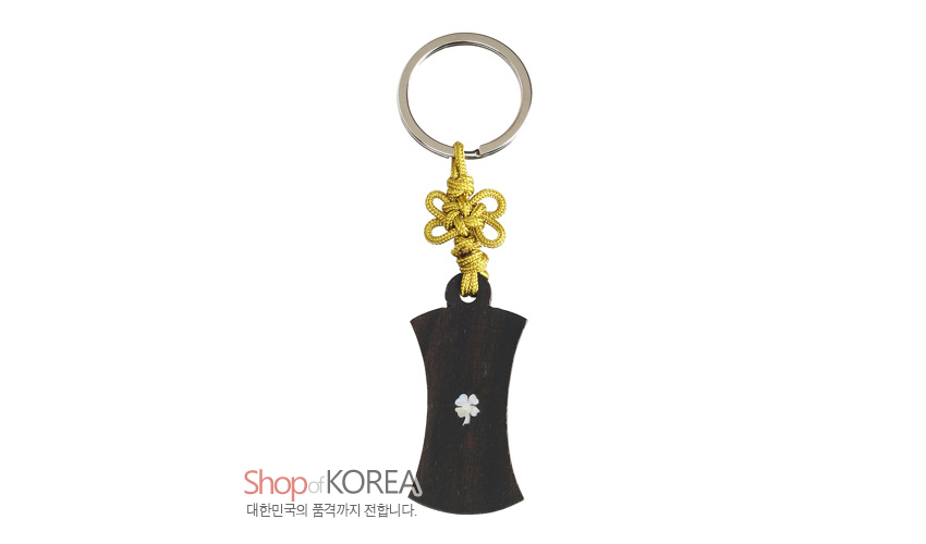 [텍스트: Shop of KOREA 대한민국의 품격까지 전합니다.] 흑단 몸체에 작은 자개 복식당초 문양을 상감하고 노란색 전통 매듭과 금속 링을 더한 열쇠고리 이미지 설명