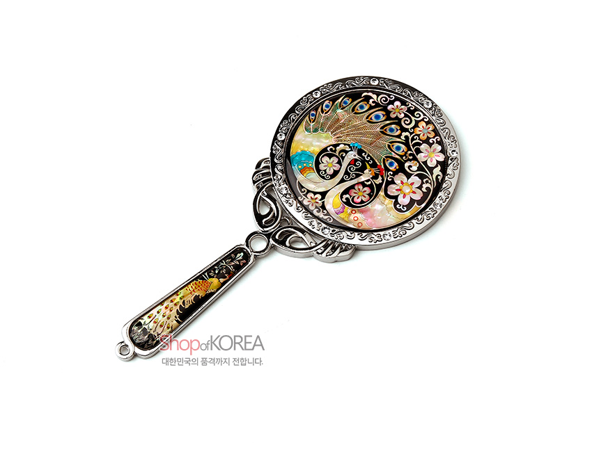 [텍스트: shopofKOREA 대한민국의 품격까지 전합니다.] 흑색 바탕 위 자개 상감 기법으로 공작과 꽃문양을 섬세하게 표현하고 금속 장식 테두리와 손잡이가 조화를 이룬 원형 손거울 이미지 설명