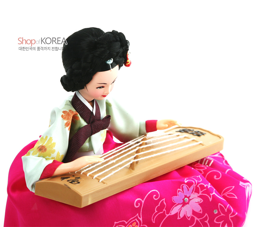 [텍스트: Shop of KOREA, 대한민국의 품격까지 전합니다] 분홍색 꽃문양 비단 치마와 연두빛 저고리를 입고 나무 재질 가야금을 연주하는 전통 한복 인형 장식 모습