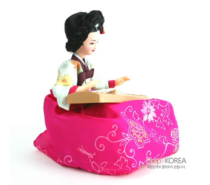 [텍스트: Shop of KOREA 대한민국의 품격까지 전합니다.] 분홍색 꽃문양 비단 치마와 연두색 꽃무늬 저고리를 입고, 나무 재질 가야금을 연주하는 한복 인형 장식 모습