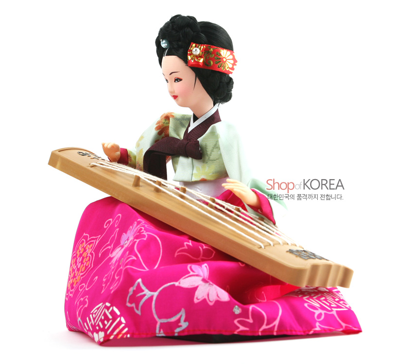 [텍스트: Shop of KOREA 대한민국의 품격까지 전합니다.] 분홍 비단 치마에 꽃·나비 문양, 연두빛 저고리와 자수 머리띠, 나무 재질 가야금을 표현한 전통 한복 인형 모습
