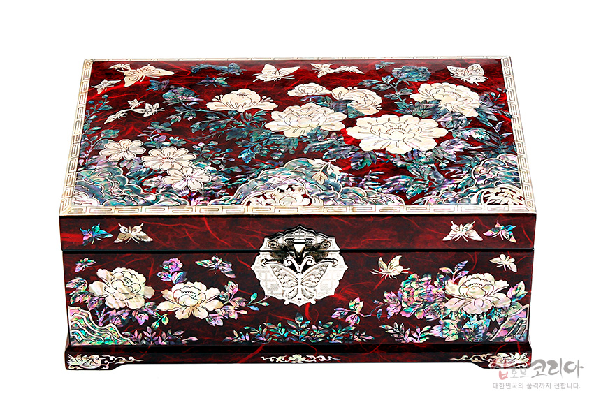 [텍스트: 샵오브코리아 대한민국의 품격까지 전합니다.] 붉은 옻칠 한지 바탕에 자개 상감 기법으로 목단과 나비 문양을 촘촘히 장식하고 금속 잠금장치를 더한 직사각형 보석함 이미지 설명