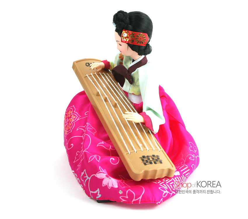 [텍스트: Shop of KOREA 대한민국의 품격까지 전합니다.] 자개 느낌의 나무 가야금을 안고, 꽃문양 짙은 분홍 비단 치마와 연두색 저고리를 갖춘 전통 한복 인형 장식