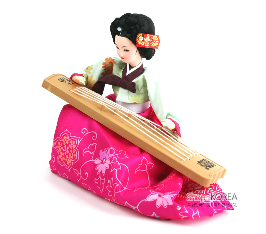 [텍스트: 샵오브코리아 대한민국의 품격까지 전합니다.] 분홍색 꽃무늬 비단 치마와 연두 저고리, 나무 재질 가야금과 비녀 장식을 더한 한복 인형 장식