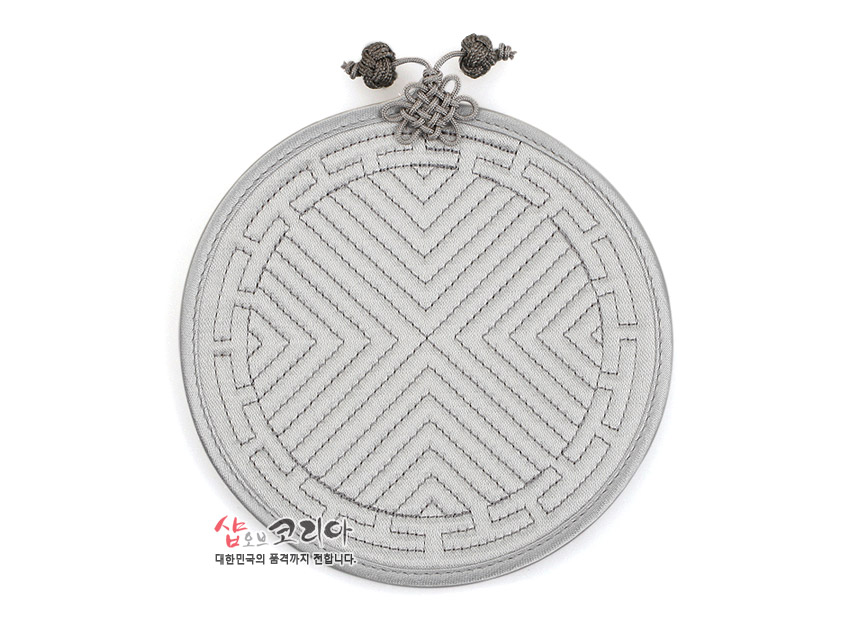[텍스트: 샵오브코리아 대한민국의 품격까지 팝니다.] 파스텔 그레이 색상 원형 천 소재에 전통 누비 기법으로 기하학 문양을 넣고 윗부분에 매듭 장식을 더한 컵받침 이미지 설명