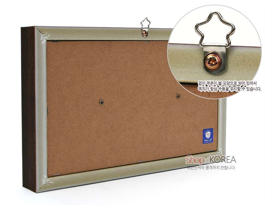 [텍스트: 걸이 부분이 별 모양으로 되어 있어서 액자가 항상 수평을 유지할 수 있습니다. Shop KOREA 대한민국의 품격까지 전합니다.] MDF 뒷판과 금속 프레임, 별 모양 금속 고리를 사용한 벽걸이 액자 뒷면 구조 설명 이미지