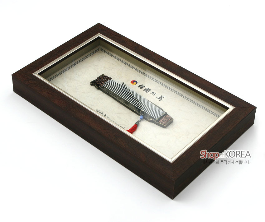 [텍스트: 韓國의美, 가야금(Gayageumum), ShopKOREA, 대한민국의 품격까지 전합니다.] 짙은 목재 액자 속 금속 가야금 모형과 청색 구슬·홍색 술 장식, 전통 문양 테두리와 태극 문양 배치된 디자인 액자 구성