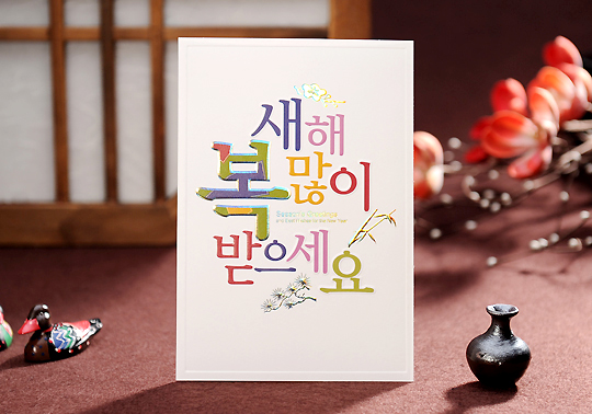 [텍스트: 새해 복 많이 받으세요] 화이트 배경 위 다채로운 색감의 서체로 구성된 연하장, 대나무와 매화 일러스트가 더해진 단정한 디자인의 새해 카드 이미지