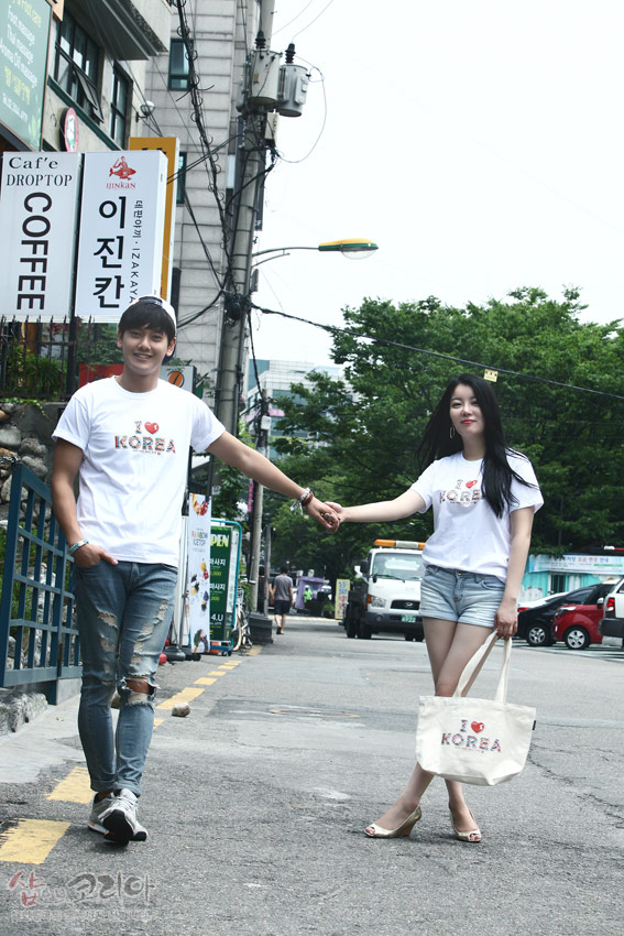 [텍스트: I ♥ KOREA] 흰색 면 티셔츠와 가방에 3D 입체발포 기법으로 표현된 하트와 전통문양 레터링 장식이 돋보이는 캐주얼 거리 패션 이미지