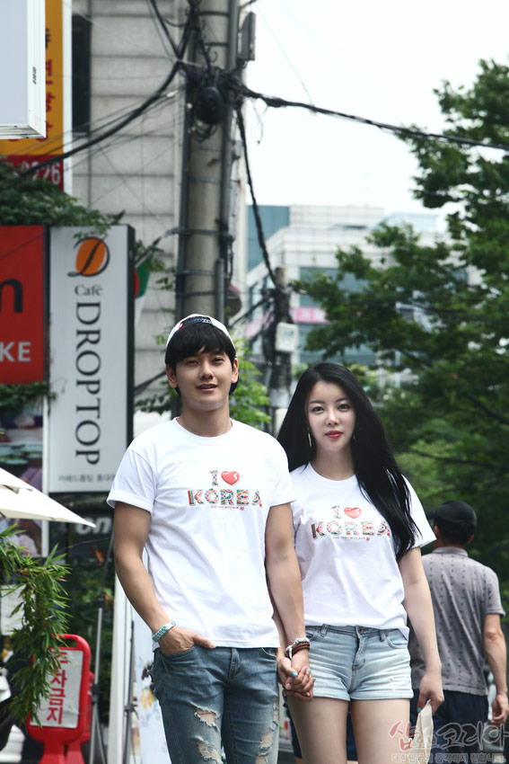 [텍스트: I ♥ KOREA] 흰색 면 반팔 티셔츠 위 알록달록한 전통 문양을 활용한 3D 입체발포 영문 문구와 하트 장식이 돋보이는 캐주얼 커플 연출 이미지 설명