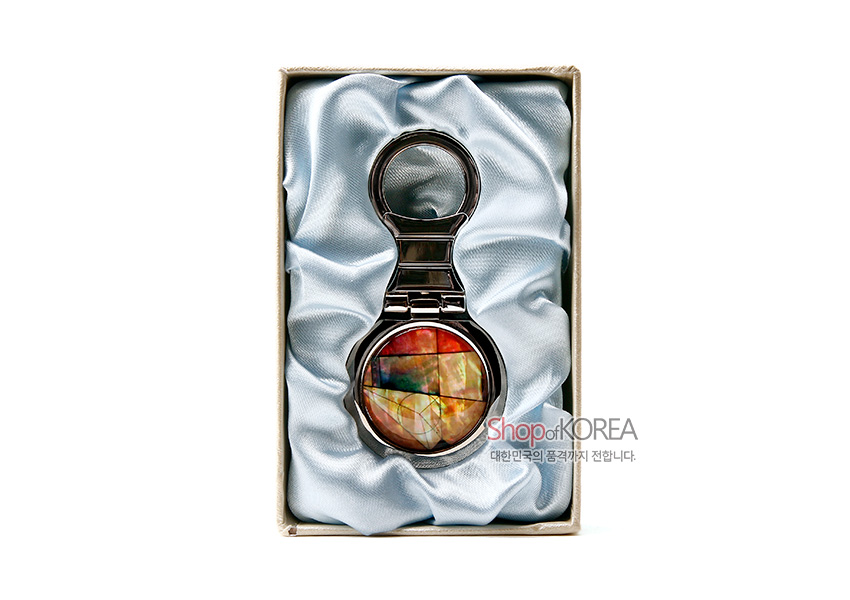 [텍스트: Shop of KOREA 대한민국의 품격까지 전합니다.] 은은한 광택의 자개를 상감한 옅은 조각보 원형 문양과 금속 프레임이 조화를 이루는 열쇠고리 디자인