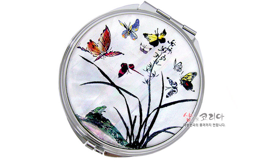 [텍스트: 샾오브코리아 대한민국의 품격까지 전합니다.] 자개 바탕 위 옻칠 기법으로 표현된 난초와 다채로운 나비 문양이 어우러진 원형 금속 손거울 디자인
