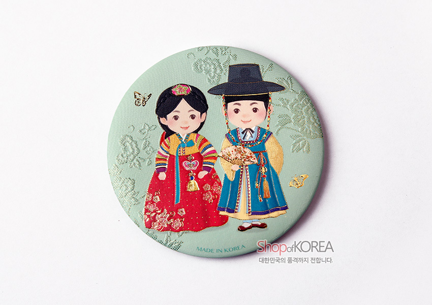 [텍스트: MADE IN KOREA, Shop of KOREA 대한민국의 품격까지 전합니다.] 파스텔 민트색 금속 원형 거울 위 전통 혼례 예복을 입은 남녀 일러스트와 나비, 연꽃문 양각 장식 디자인