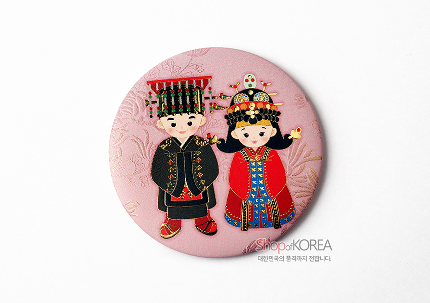 [텍스트: ShopofKOREA 대한민국의 품격까지 전합니다.] 연분홍 색상의 양각 전통문양 배경 위 금속 재질, 전통 예복을 입은 신랑·신부 일러스트 장식 원형 손거울 디자인