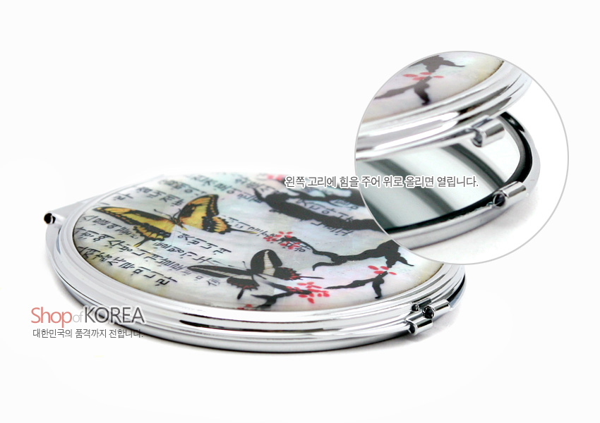 [텍스트: Shop of KOREA / 대한민국의 품격까지 전합니다 / 왼쪽 고리에 힘을 주어 위로올리면 열립니다.] 자개 바탕 위에 옻칠로 표현한 매화나무와 나비, 한글 서체 문양이 어우러진 원형 금속 휴대용 양면 손거울 디자인