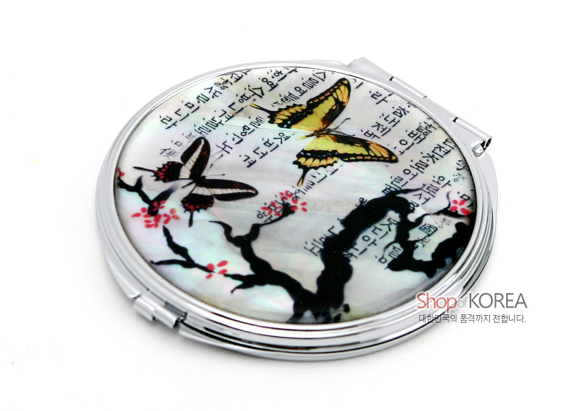 [텍스트: Shop of KOREA 대중문화의 품격까지 전합니다.] 자개 바탕 위 옻칠 기법으로 매화나무와 나비, 흑백 한글 서체 문양을 담은 원형 금속 손거울 이미지
