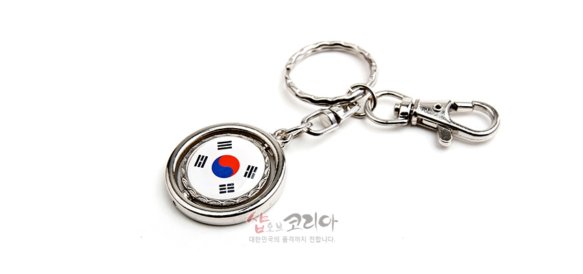 [텍스트: 샵오브코리아 대한민국의 품격까지 전합니다.] 금속 재질의 원형 테두리 안에 흰색 바탕 태극기 문양을 넣은 열쇠고리 디자인